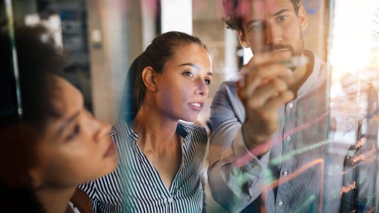 Business professionals analyzing data on a transparent board, with a woman in striped shirt focused on charts and graphs.