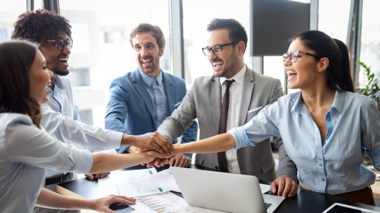 team of five people in a circle, hands in the middle for unity
